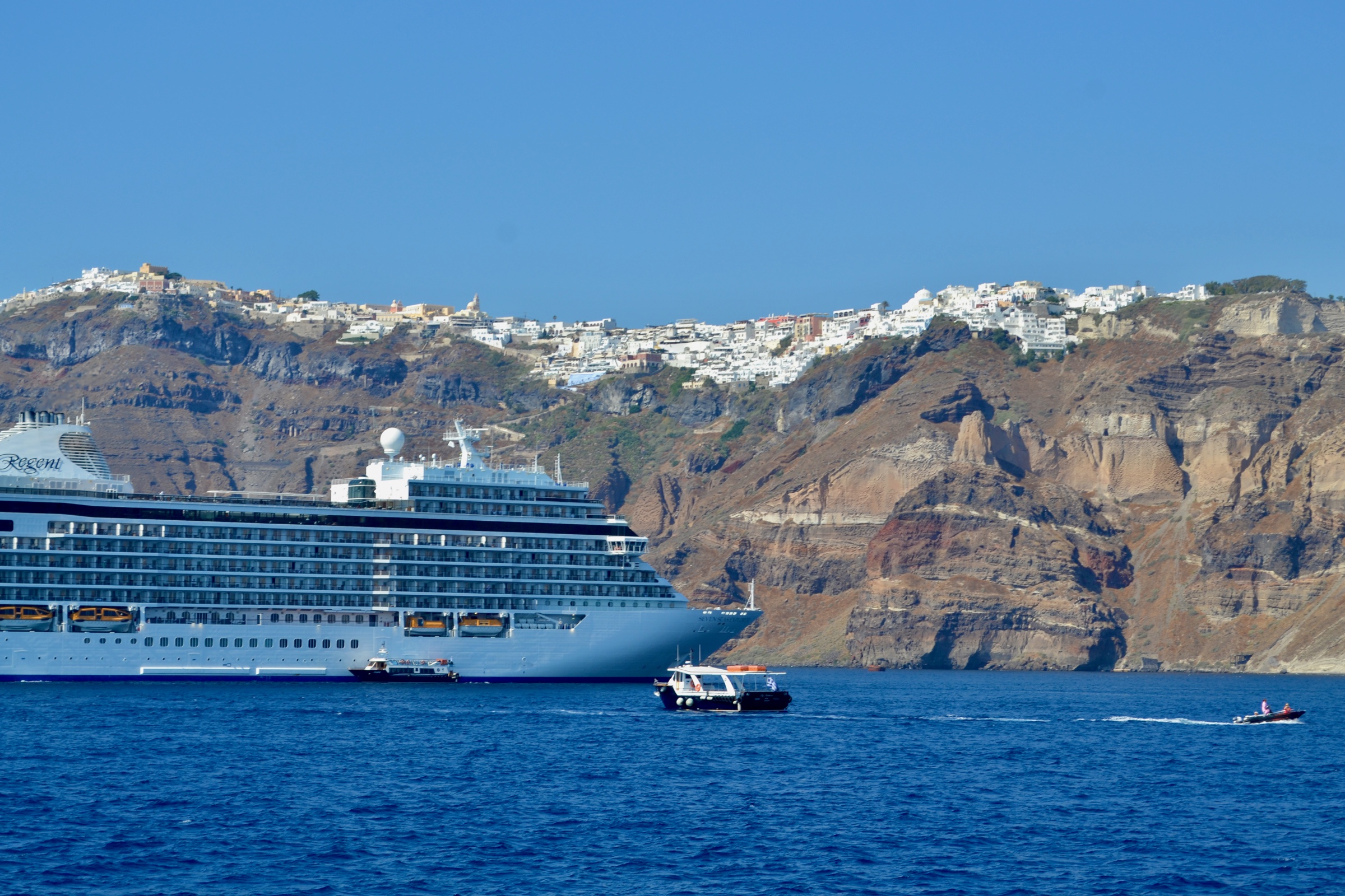 A cruise ship sailing through the Santorini caldera beneath the island's whitewashed villages